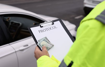 Photo of Police officer with bribe and clipboard near car outdoors, closeup