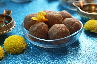 Photo of Diwali celebration. Yellow flowers and tasty Indian sweets on shiny light blue table, closeup