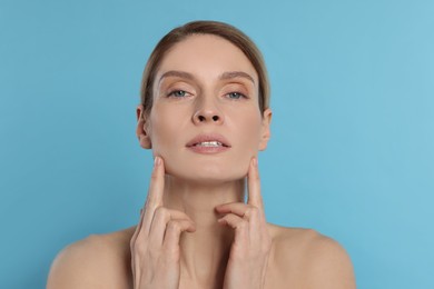 Woman massaging her face on turquoise background