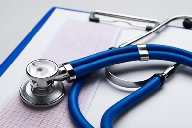 Photo of Stethoscope, clipboard and cardiogram paper on white background, closeup
