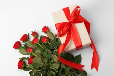 Beautiful gift box with bow and red roses on white background, top view