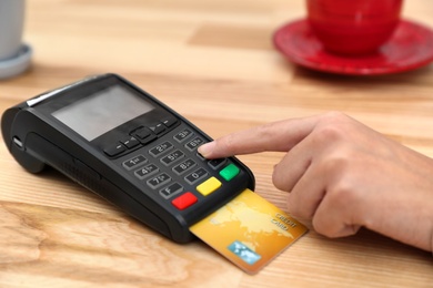 Woman using card machine for non cash payment at table, closeup