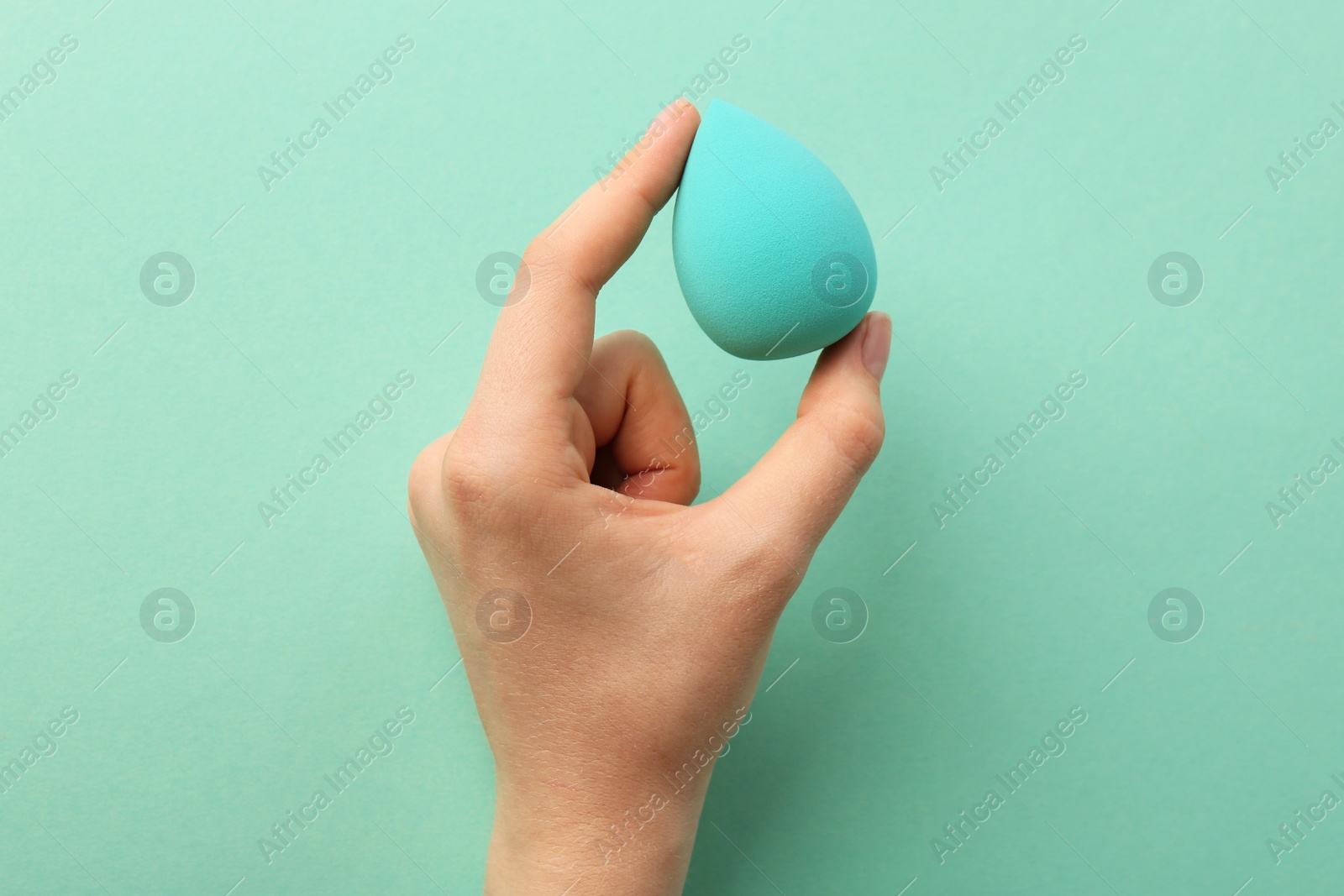 Photo of Woman with makeup sponge on mint color background, top view