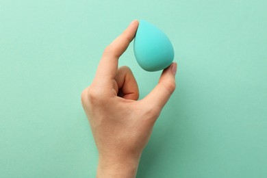Photo of Woman with makeup sponge on mint color background, top view