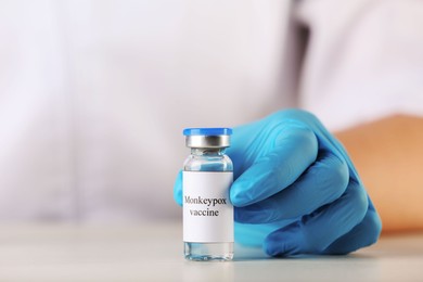 Nurse with glass vial of monkeypox vaccine at table, closeup