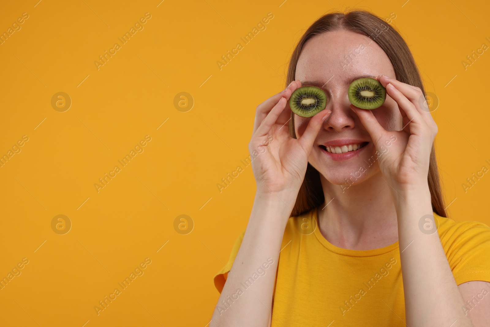 Photo of Young woman holding halves of kiwi near her eyes on yellow background. Space for text