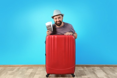 Photo of Man with suitcase and passport near color wall. Vacation travel