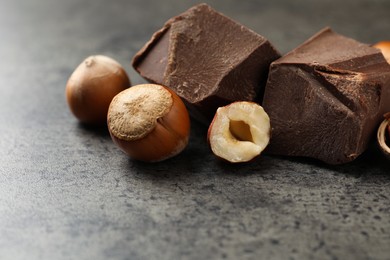 Delicious chocolate chunks and hazelnuts on grey table, closeup