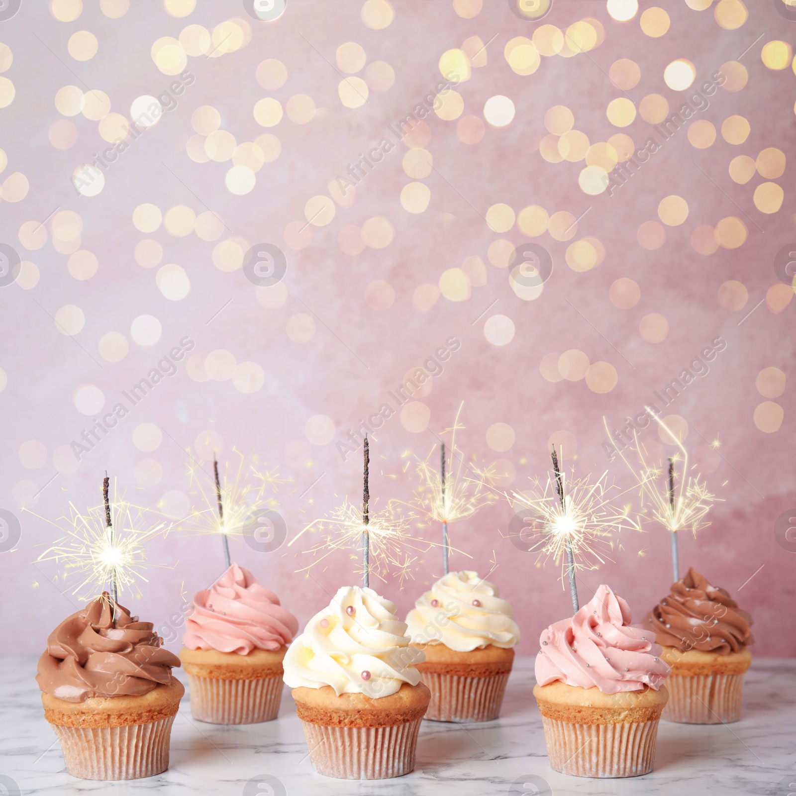 Image of Birthday cupcakes with sparklers on table against light pink background