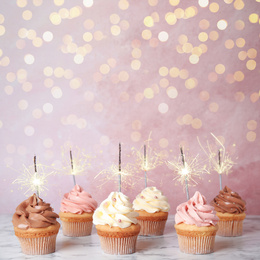 Image of Birthday cupcakes with sparklers on table against light pink background