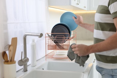 Man putting clean plate on drying rack in kitchen, closeup