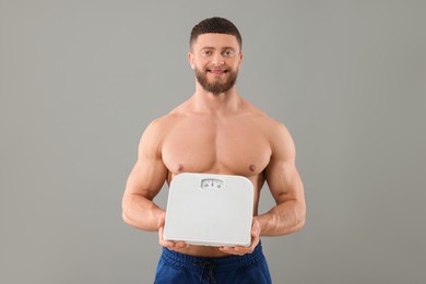 Photo of Portrait of happy athletic man holding scales on grey background. Weight loss concept