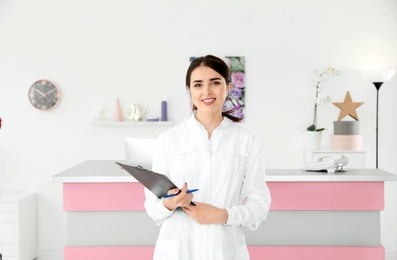 Photo of Young receptionist with clipboard at desk in beauty salon