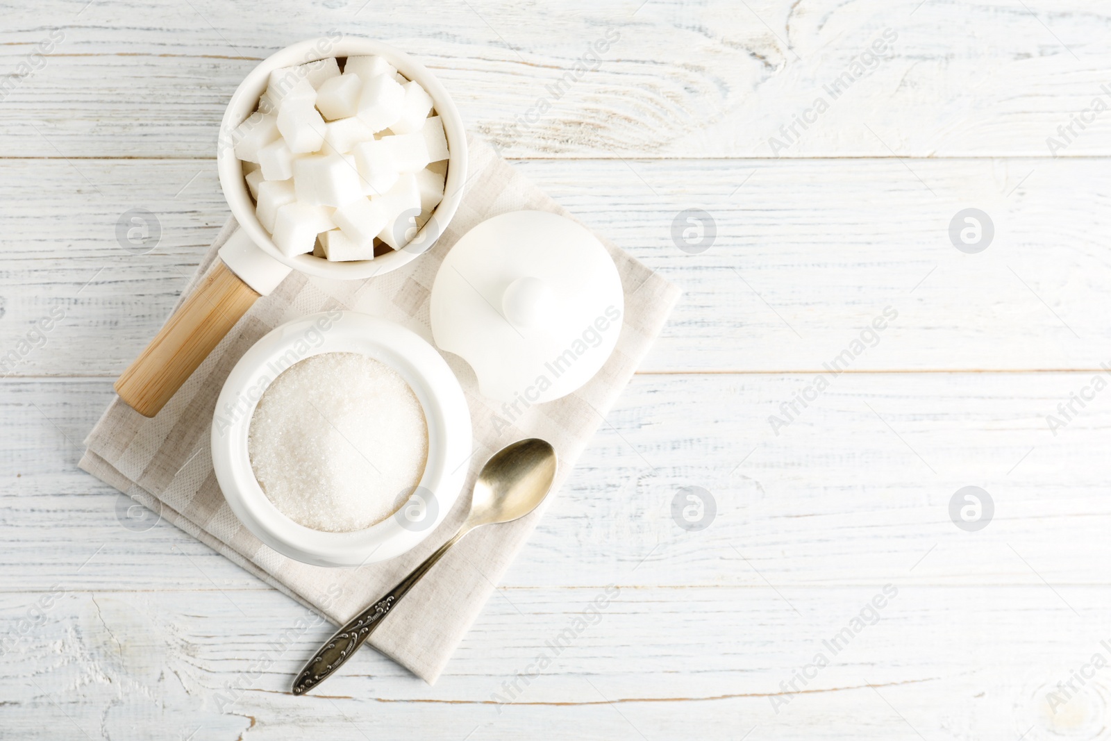 Photo of Dishware with sugar on white wooden table, flat lay. Space for text