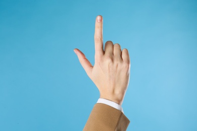 Businesswoman pointing at something on light blue background, closeup. Finger gesture