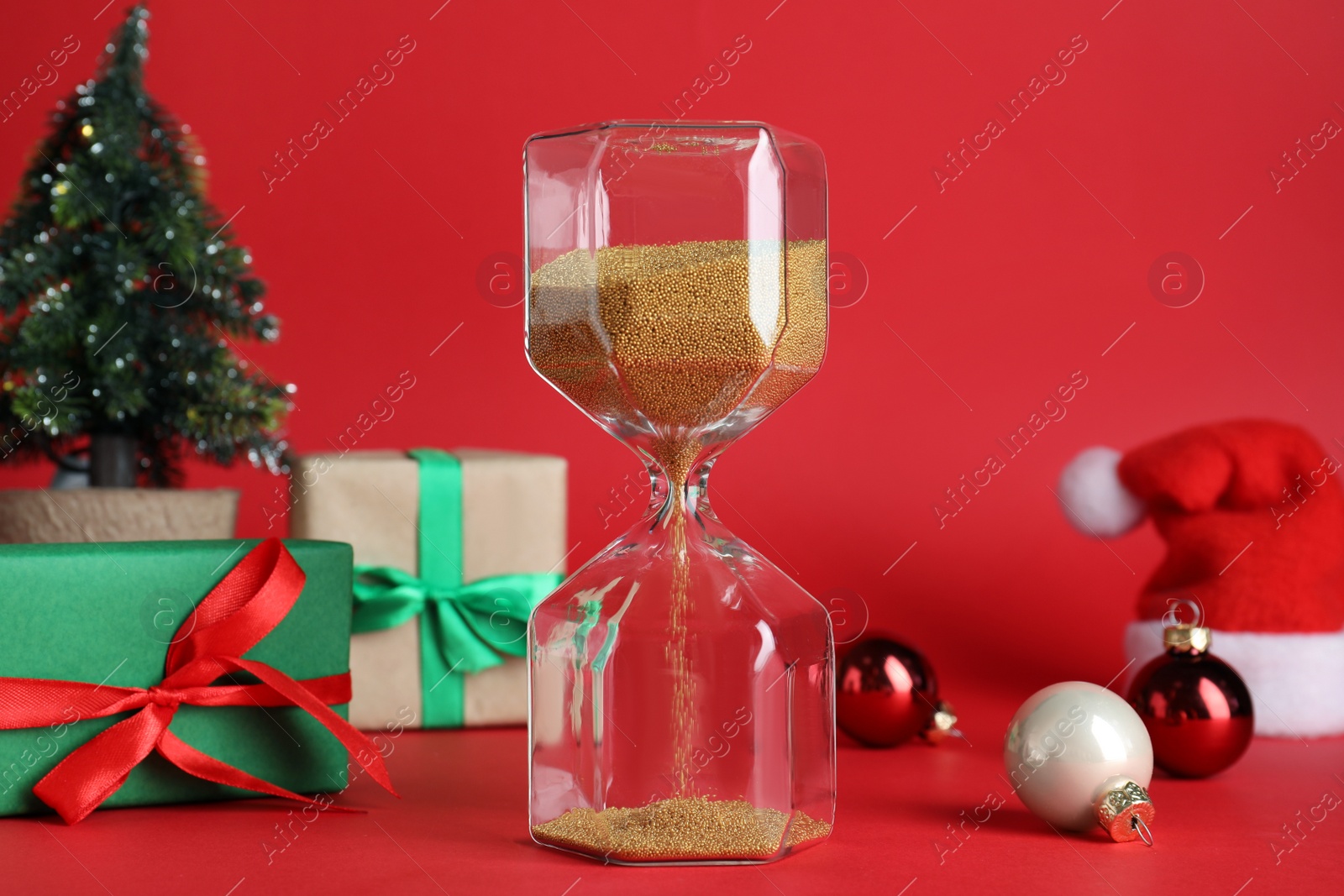 Photo of Hourglass, gifts and decor on red background. Christmas countdown