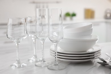 Photo of Different clean dishware, cutlery and glasses on white marble table in kitchen, closeup