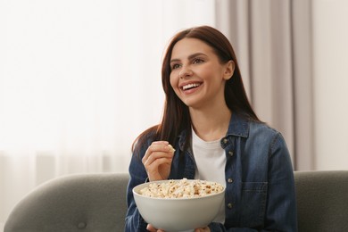 Photo of Happy woman with bowl of popcorn watching TV at home
