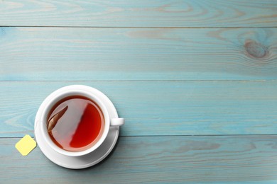 Photo of Tea bag in cup with hot drink on light blue wooden table, top view. Space for text