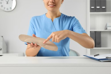 Photo of Female orthopedist showing insole at table in hospital, closeup