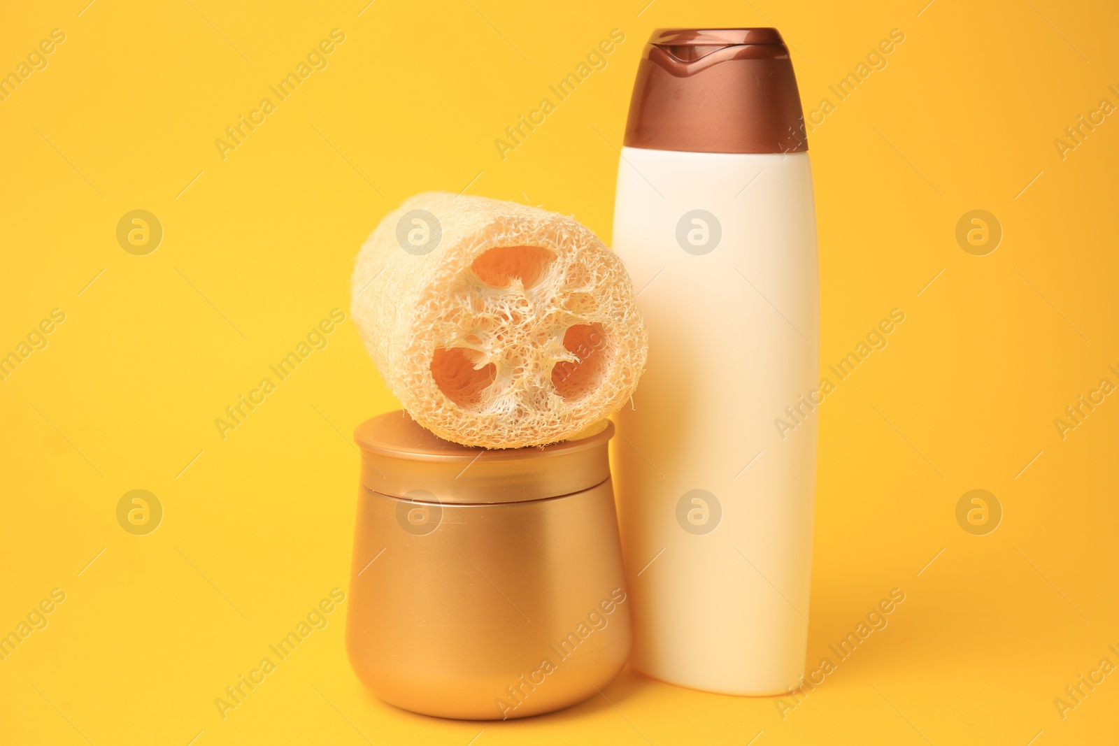 Photo of Natural loofah sponge and cosmetic products on yellow background