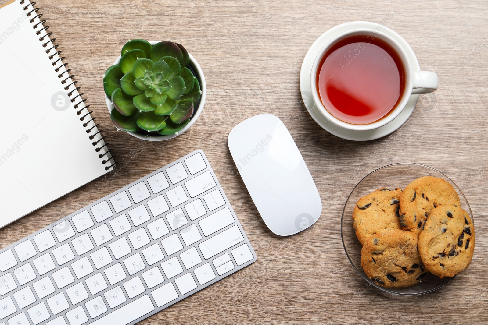 Photo of Chocolate chip cookies, tea and keyboard on wooden table at workplace, flat lay