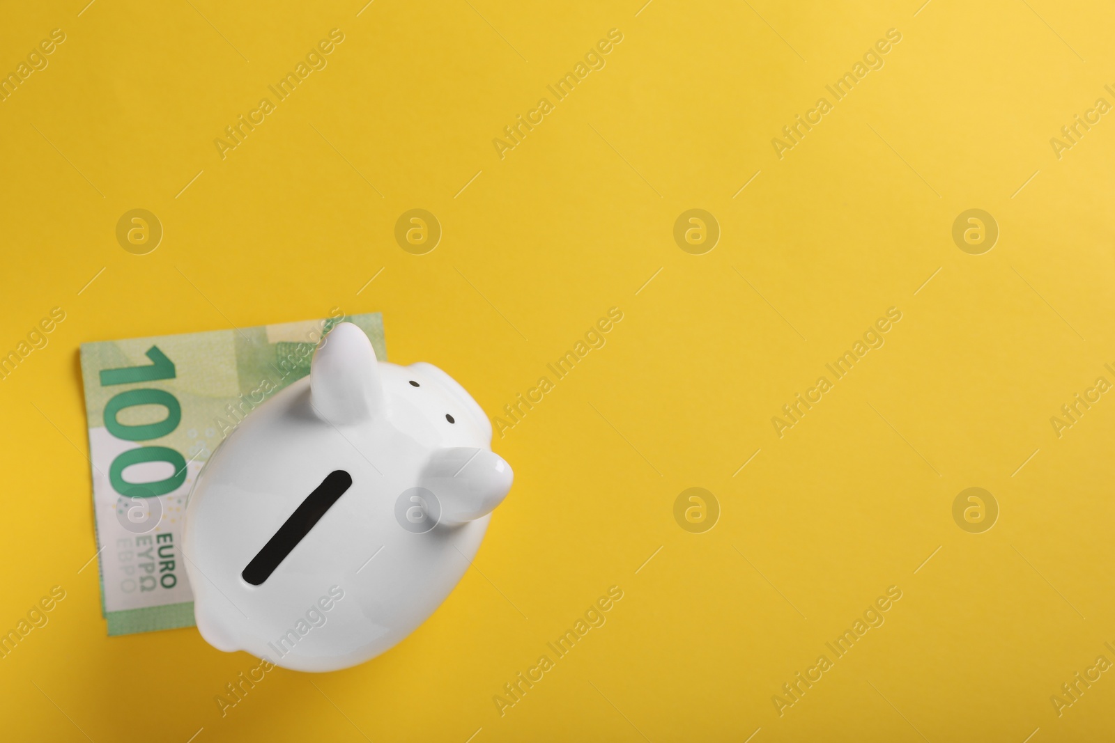 Photo of Ceramic piggy bank and euro banknote on yellow background, top view with space for text. Financial savings