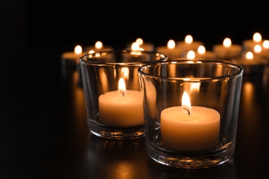 Wax candles burning on table in darkness, closeup