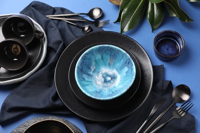 Stylish table setting. Dishware, cutlery and floral decor on blue background