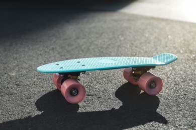 Photo of Modern light blue skateboard with pink wheels on asphalt road outdoors