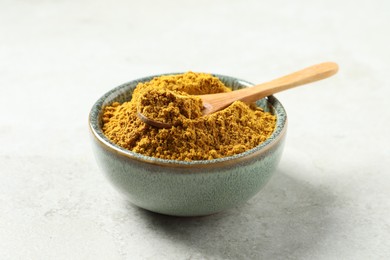 Photo of Dry curry powder in bowl and spoon on light table, closeup