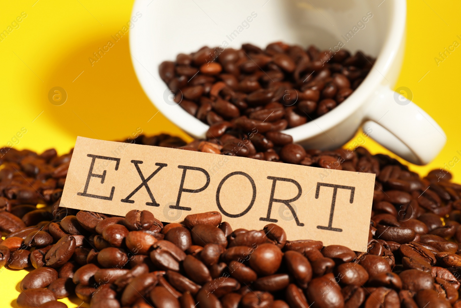 Photo of Coffee beans, white cup and card with word Export on yellow background, closeup