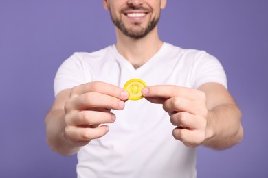 Happy man holding condom on purple background, closeup