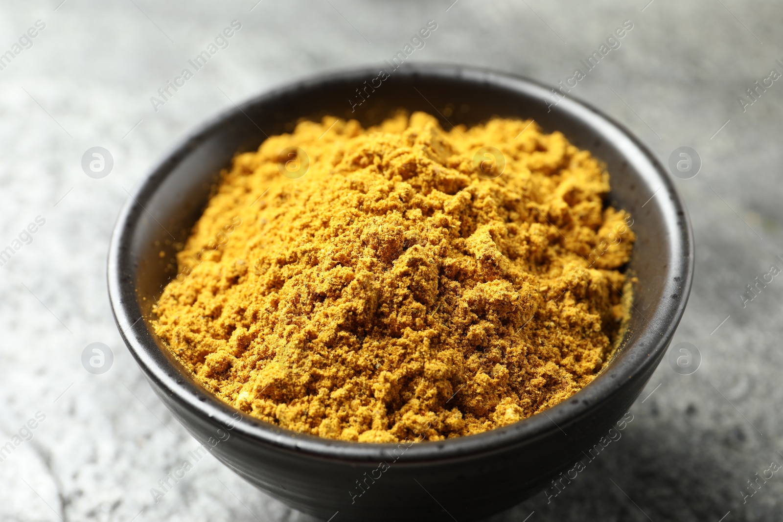 Photo of Dry curry powder in bowl on dark table, closeup