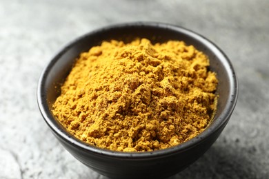 Photo of Dry curry powder in bowl on dark table, closeup