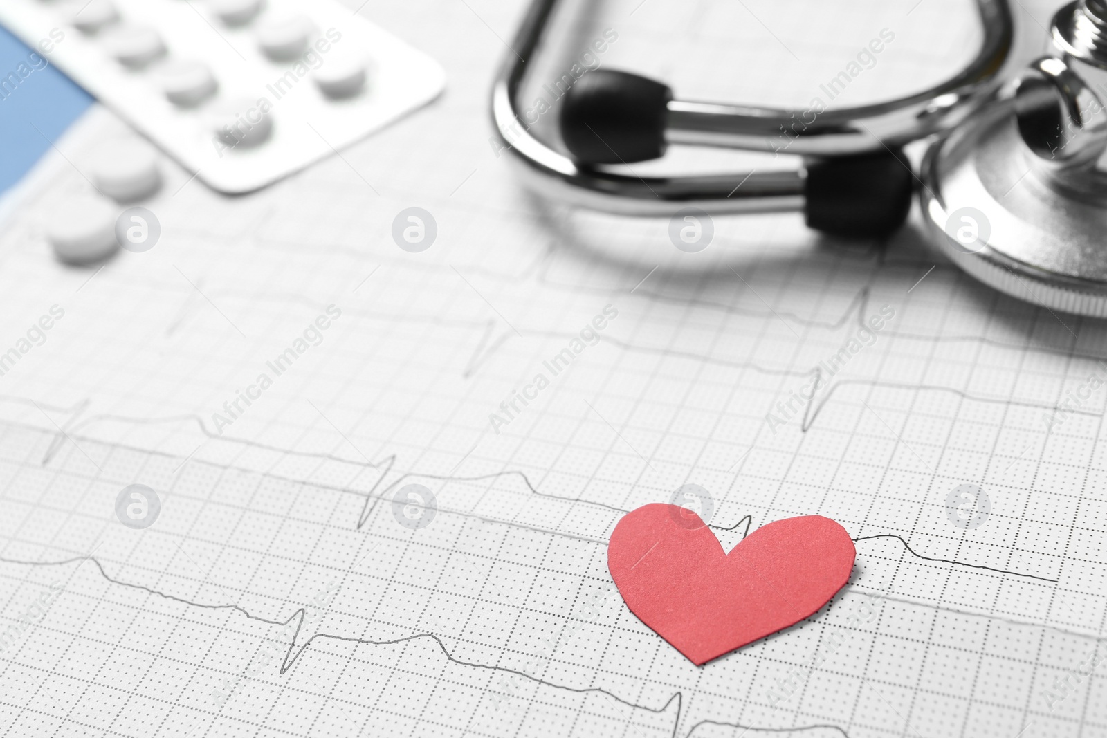 Photo of Red paper heart, pills and stethoscope on cardiogram report, closeup