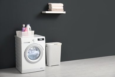 Modern washing machine, laundry basket and shelf with towels in bathroom. Space for text