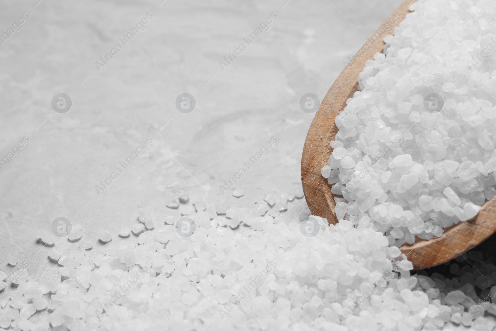 Photo of Wooden scoop and heap of natural sea salt on grey table, closeup. Space for text