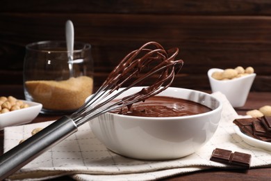 Photo of Bowl and whisk with chocolate cream on wooden table