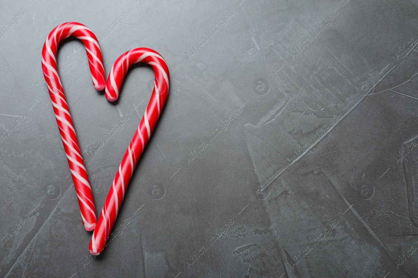 Photo of Heart made of Christmas candy canes on grey background, flat lay. Space for text