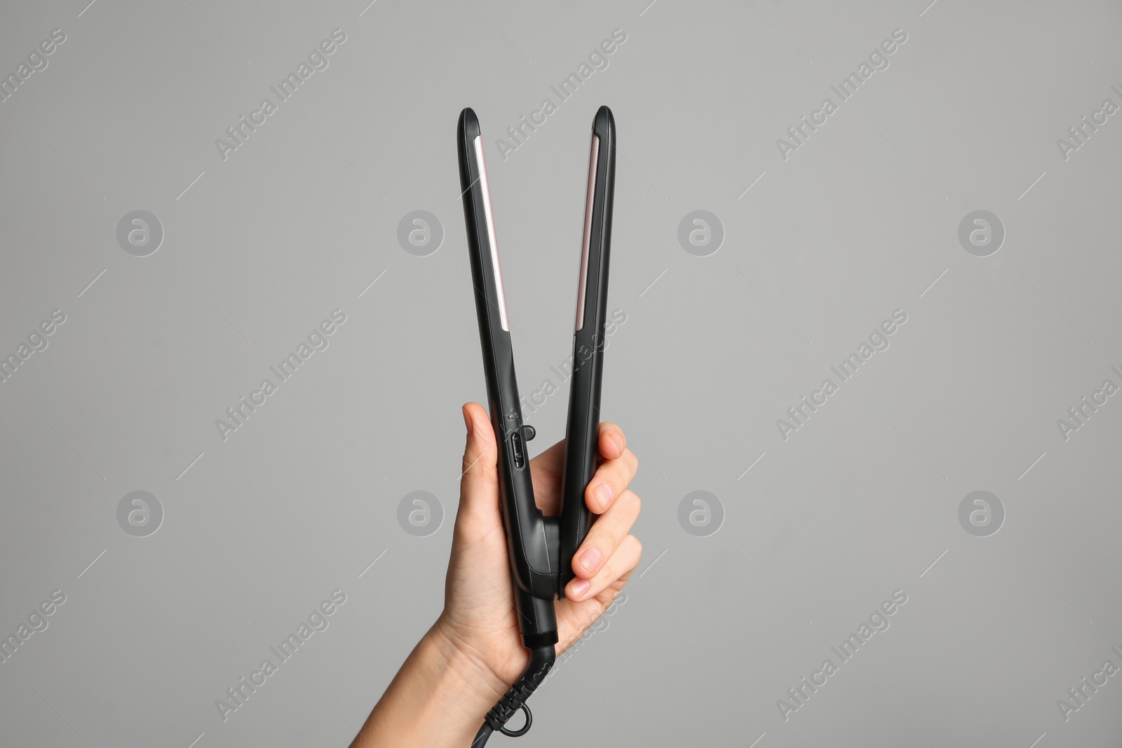 Photo of Woman holding flat hair iron on grey background, closeup