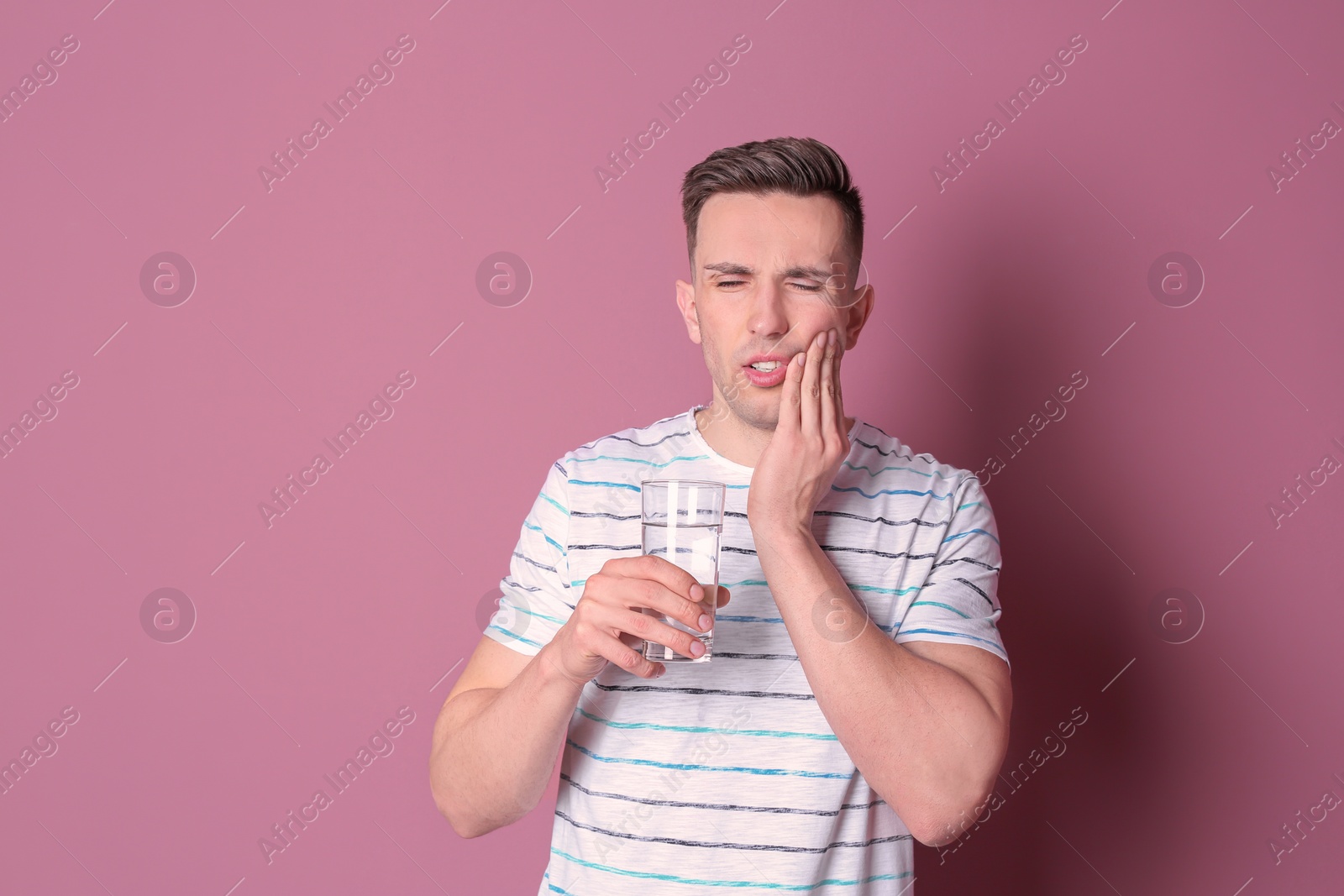 Photo of Young man with sensitive teeth and glass of cold water on color background