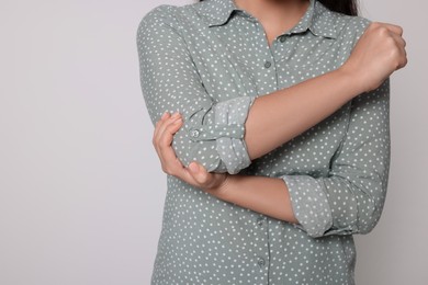 Young woman suffering from pain in elbow on light grey background, closeup with space for text. Arthritis symptoms