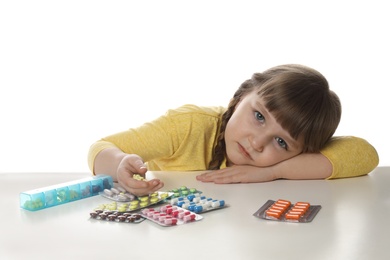 Photo of Little child with many different pills on white background. Danger of medicament intoxication
