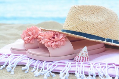 Photo of Blanket with slippers, straw hat and seashell on sand near sea, closeup Beach accessories