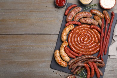 Different delicious sausages and sauces on wooden table, flat lay with space for text. Assortment of beer snacks