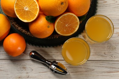Photo of Many ripe juicy oranges, squeezer and fresh juice on white wooden table, flat lay