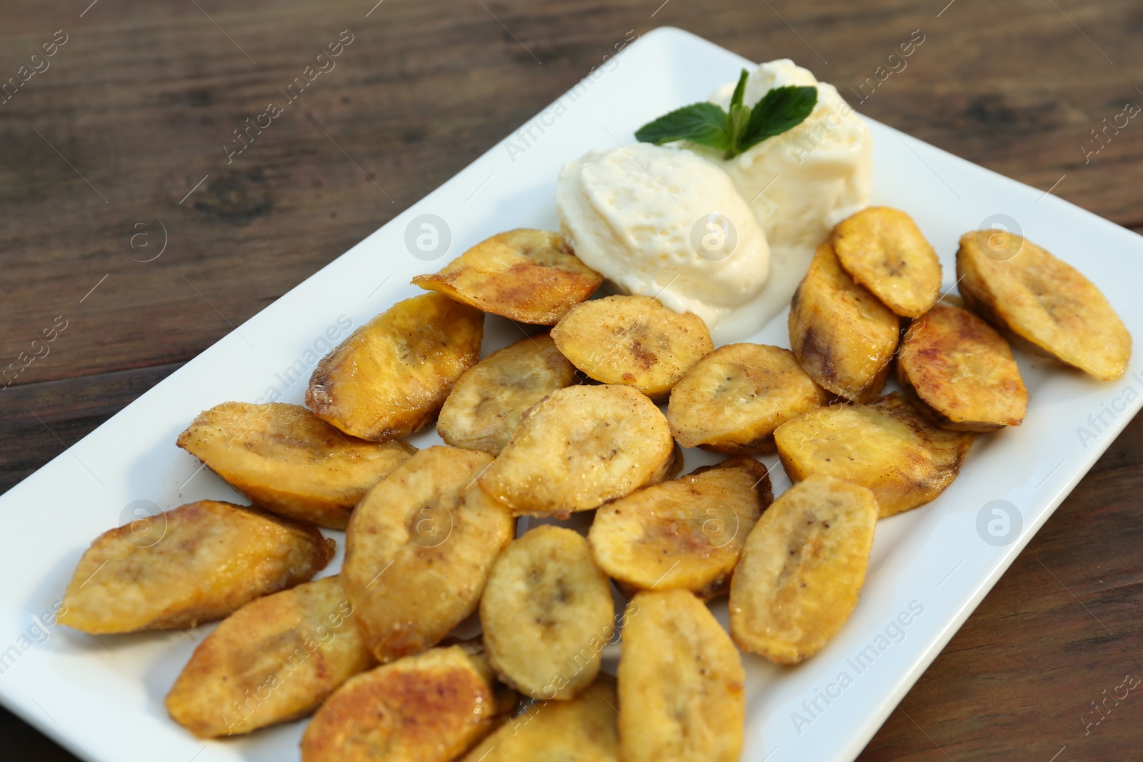 Photo of Tasty deep fried banana slices and ice cream with mint on wooden table, closeup