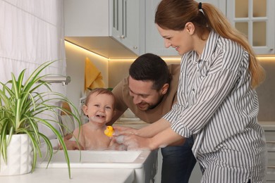 Photo of Father and mother washing their little baby in sink at home