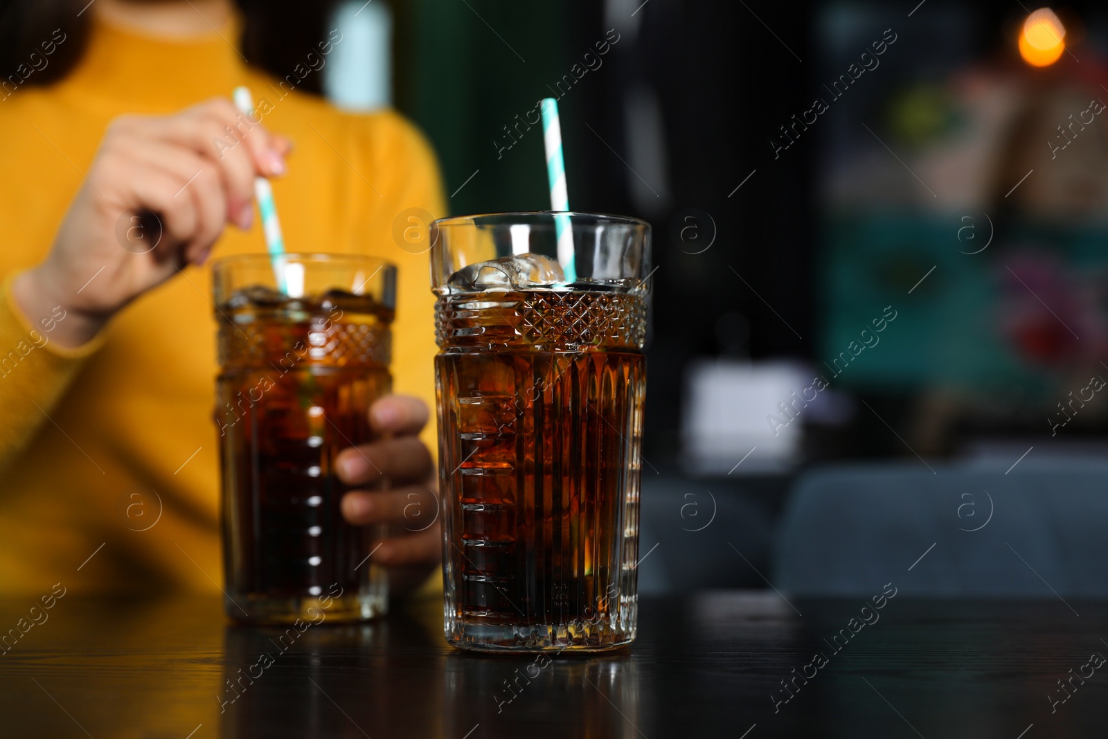Photo of Glass of refreshing cola and blurred woman on background. Space for text